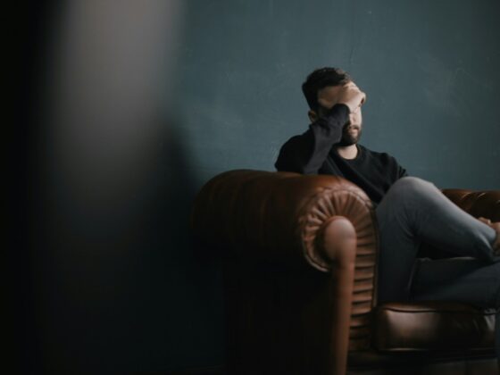 a man holds his head while sitting on a sofa