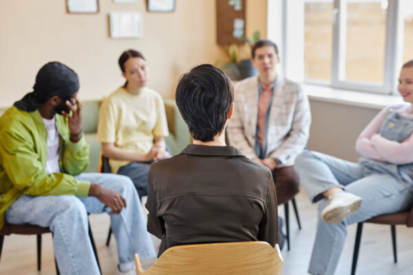 Rear view of specialist sitting on chair and talking to young people in rehab center in pennsylvania