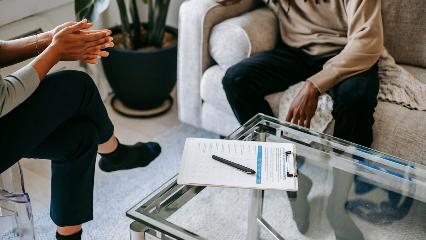 Crop anonymous African American man in casual clothes sitting on sofa and talking to female psychologist during psychotherapy session in modern studio